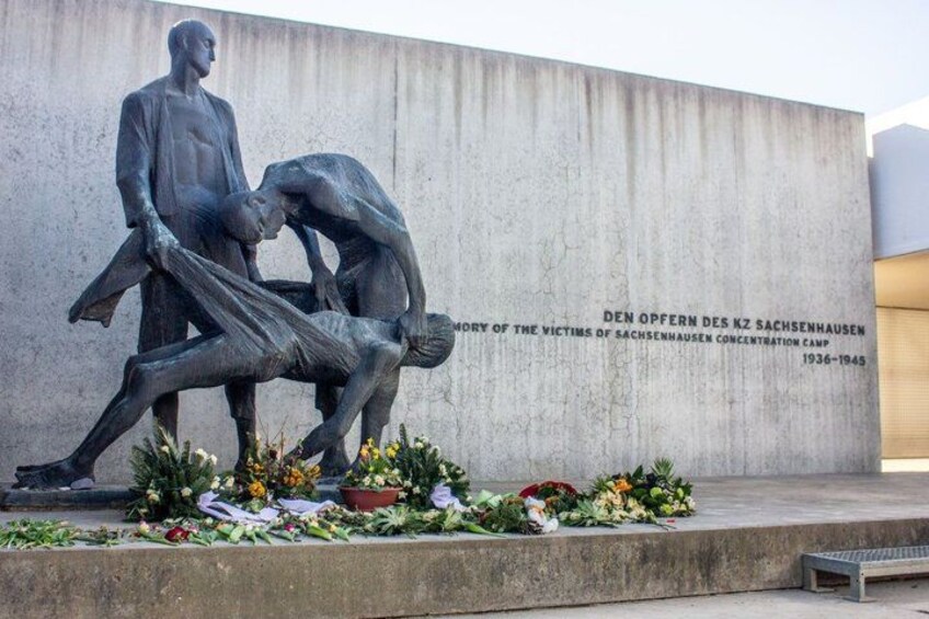 A memorial sculpture with inscriptions, flowers, and a concrete wall. 1