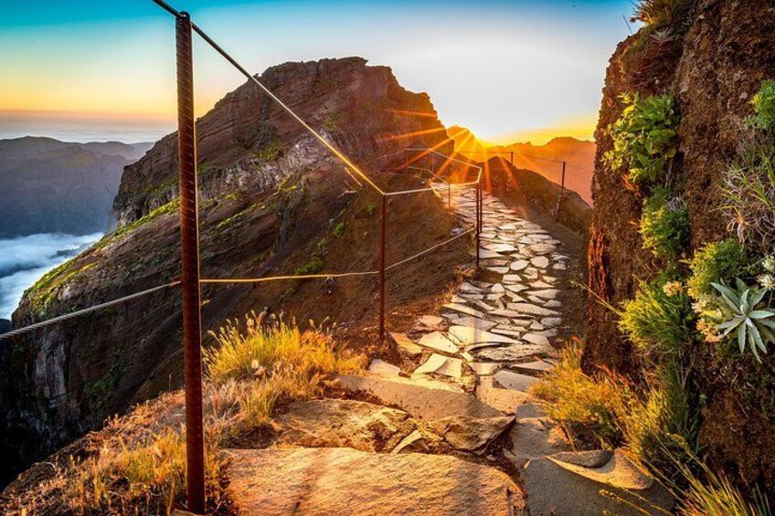 A stone pathway leading to a cliff edge with a sunset in the background. 2