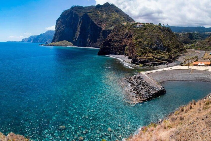 A coastal landscape with clear blue waters, a rocky outcrop, and a mountainous backdrop. 3