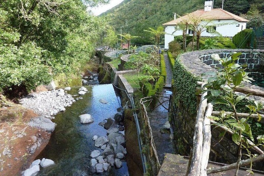 Een rivier met rotsen, een houten brug en een huis op de achtergrond. 2