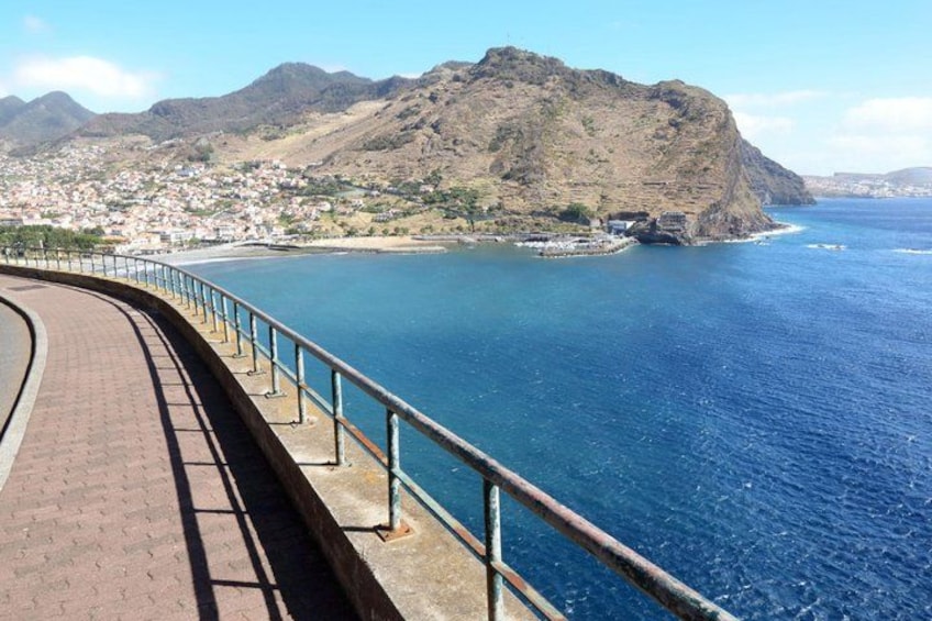 A coastal road with a metal railing, a mountain, and a town in the background. 4