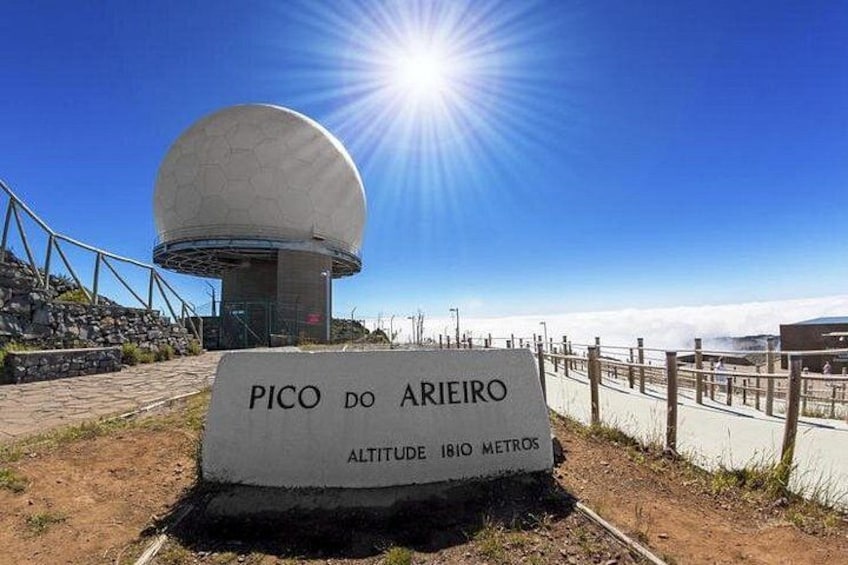 En radar kuppel med teksten 'PICO DO ARIEIRO' og et højde skilt, der viser '1810 METROS', under en klar blå himmel. 5