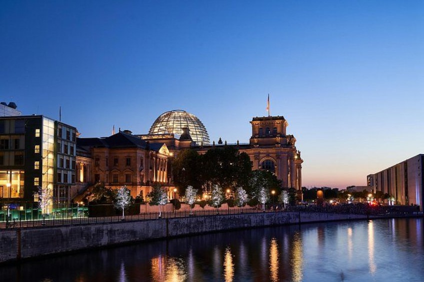 Un bâtiment historique doté d’un dôme et d’une tour horloge, dont le reflet se mire dans une étendue d’eau calme. 1