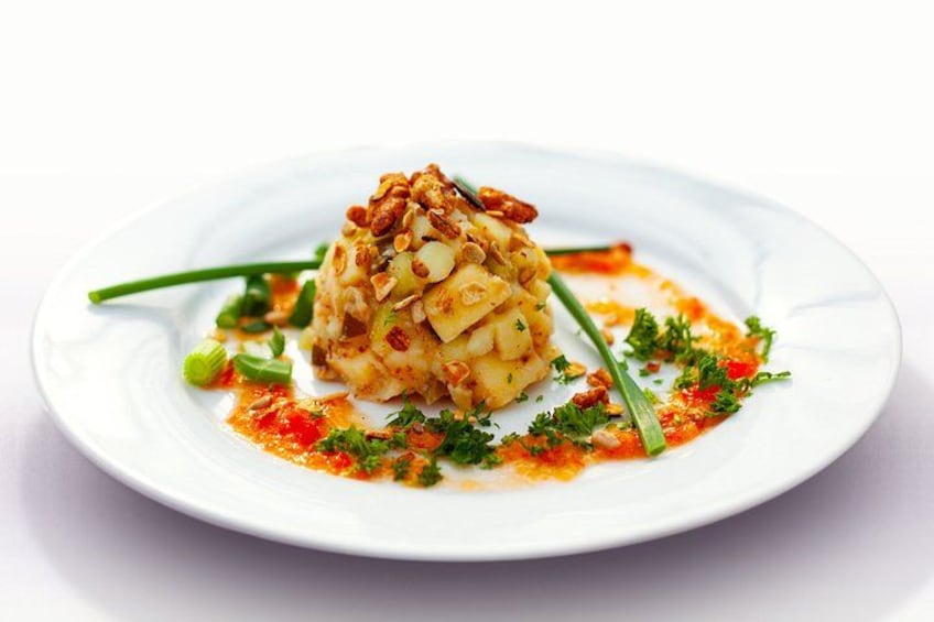 Un plat présenté sur une assiette, avec une portion généreuse de nourriture surmontée de noix, décorée d’herbes vertes et nappée d’une sauce rouge. 4