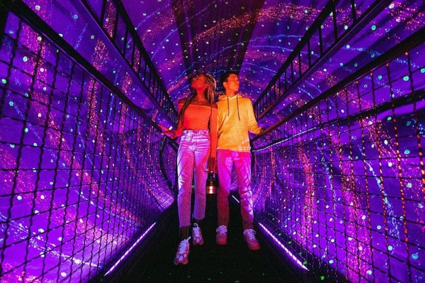 Two people walking through a tunnel with a grid of lights. 1
