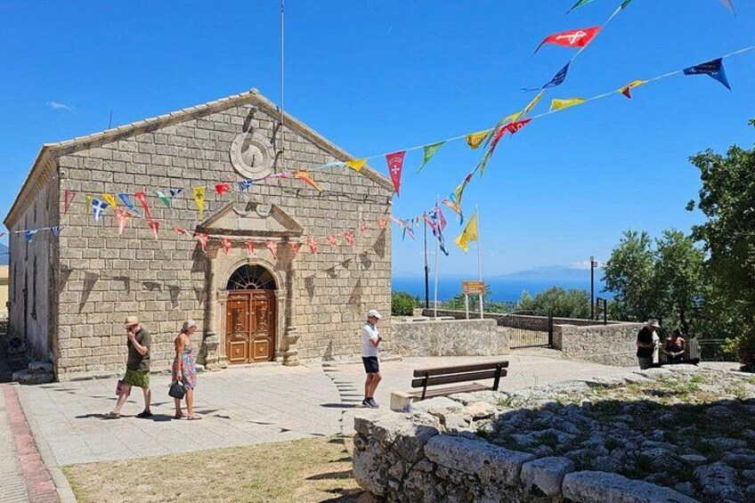 Un bâtiment en pierre doté d’une horloge, entouré d’un mur de pierre, avec des drapeaux aux couleurs vives et un ciel d’un bleu éclatant. 3