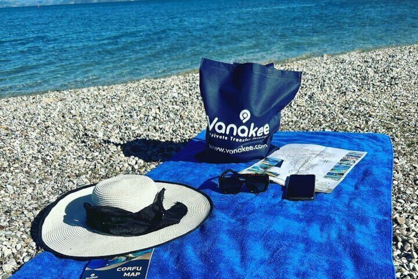 En strand med et blåt håndklæde, en stråhat, solbriller, et kort og en VanNeke tote taske. 5