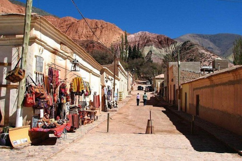 A narrow street with shops on one side and mountains in the background. 4