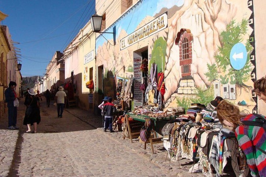 A cobblestone street with market stalls selling textiles and crafts. 3