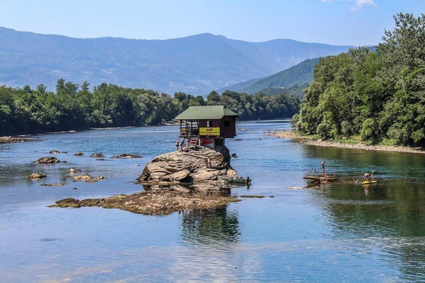 Un río con una pequeña estructura de madera sobre una roca, rodeado de vegetación exuberante y montañas al fondo. 3