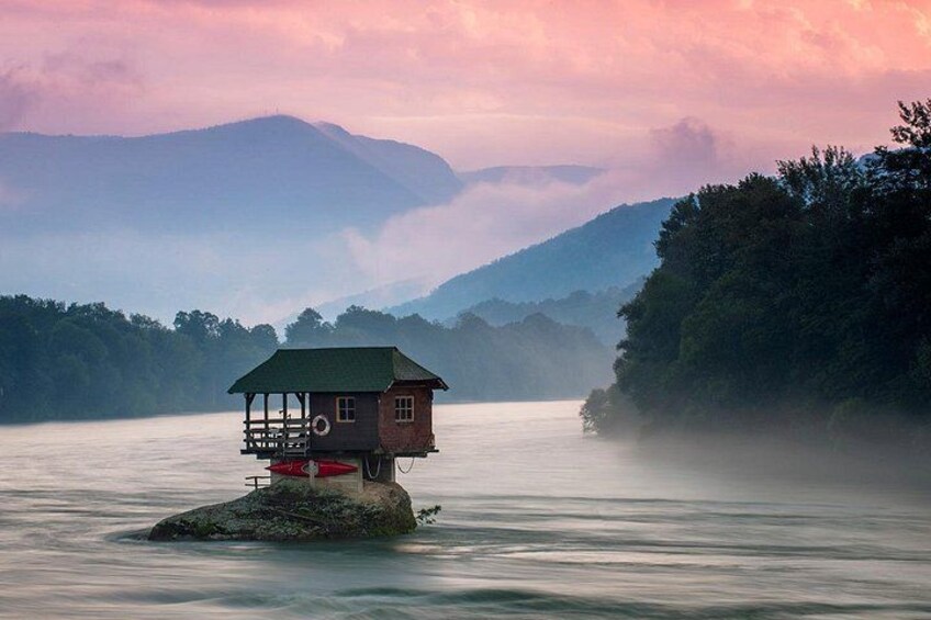 A wooden house on a rock in a calm river surrounded by mountains and trees. 2