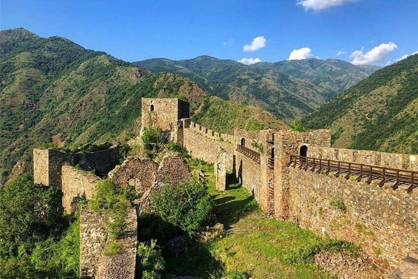 A historical stone wall with towers and battlements, surrounded by lush green hills and mountains. 1