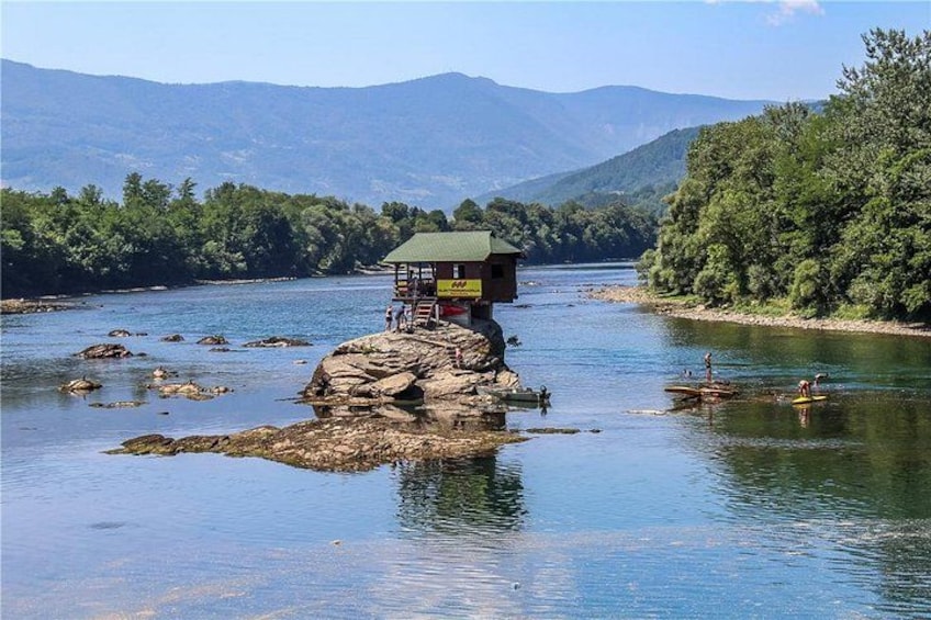 Ein Fluss mit einer hölzernen Konstruktion auf einem Felsen, umgeben von Bäumen und Bergen. 3