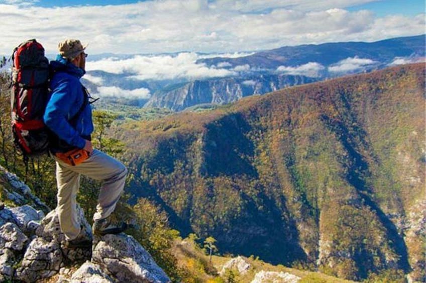 Ein Wanderer auf einem Bergrücken mit Blick auf ein Tal, eine bewaldete Landschaft und ferne Berge. 5