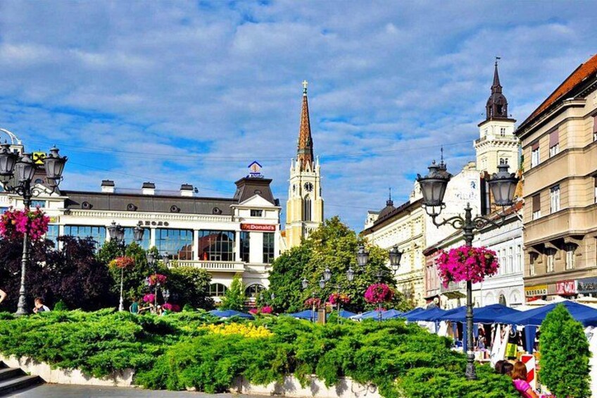 Ein historischer Stadtplatz mit einem markanten Kirchturm, üppigem Grün und traditioneller Architektur. 1