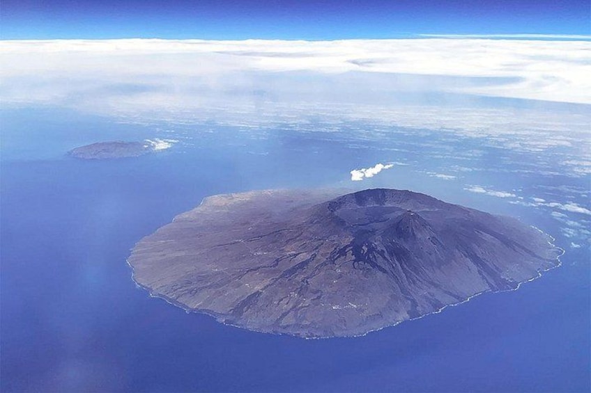 An aerial view of a volcanic island with a central peak, surrounded by a vast ocean. 1