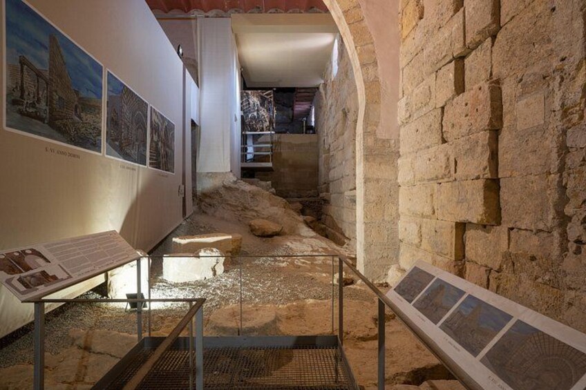 An archaeological site with stone walls, a staircase, and informational displays. 2
