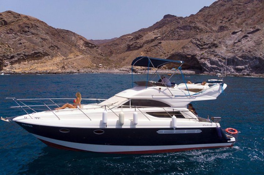 A black and white boat with a canopy, docked near rocky hills. 1