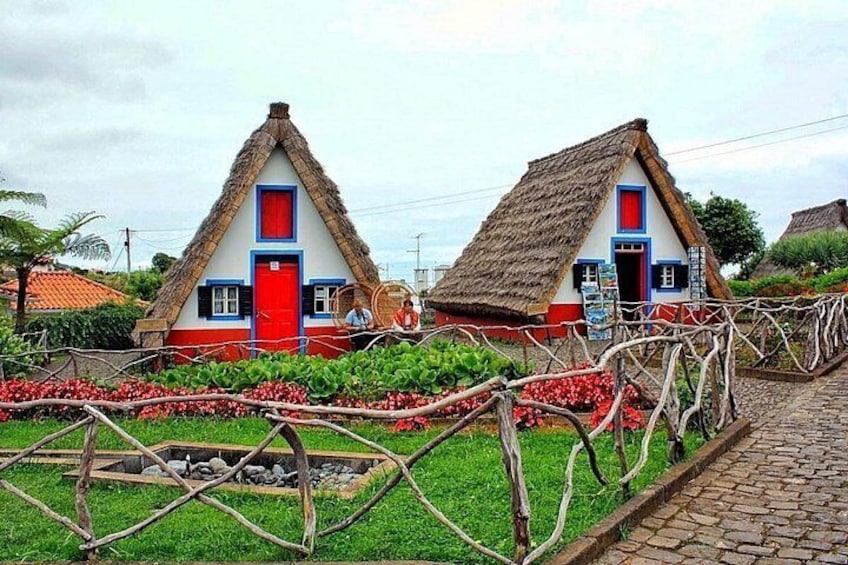 Two thatched-roof houses with red doors and blue trim, surrounded by a garden with red flowers and a cobblestone path. 3