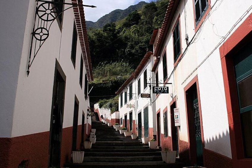 A narrow street flanked by buildings with red and white facades, leading up a hill with greenery in the background. 4