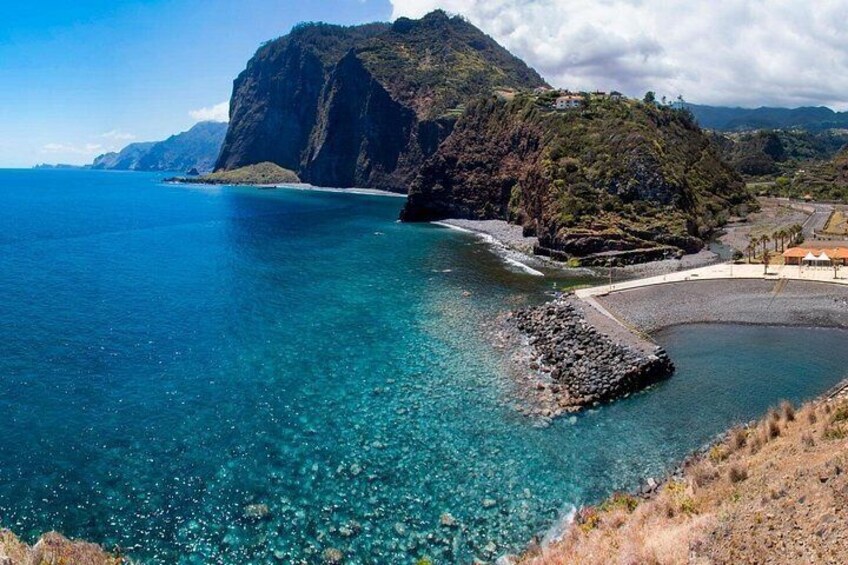 Un paisaje costero con aguas azules cristalinas, afloramientos rocosos y una imponente cadena montañosa al fondo. 2