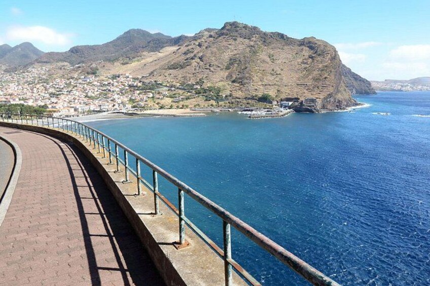 A coastal road with a metal railing, a mountain, and a town in the background. 5