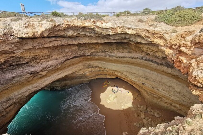 A coastal cave entrance with layered rock formations and a sandy beach. 4