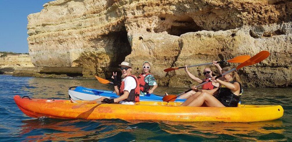 A group of people kayaking on a calm sea with rocky cliffs in the background. 2
