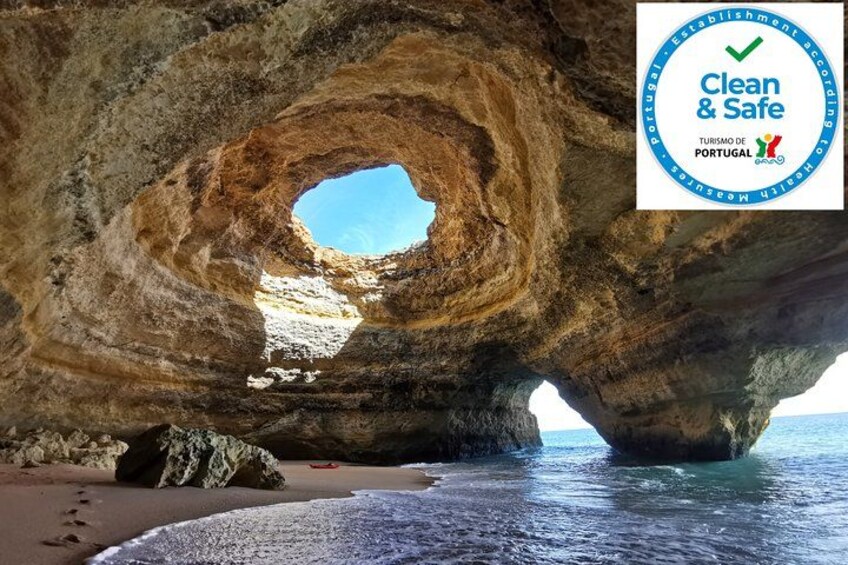 En naturlig klippeformation med en rund åbning, en sandstrand og havet. 5