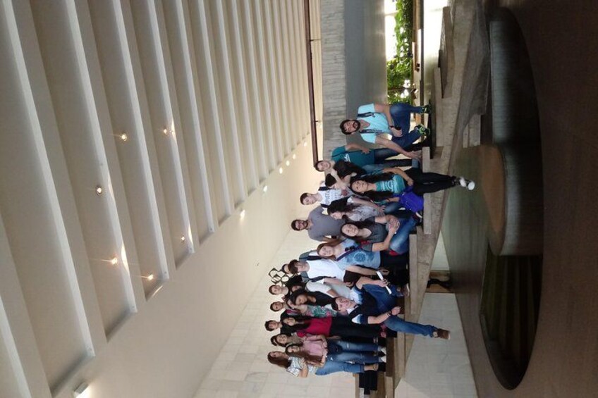 A group of people standing in a modern architectural space with white columns and a reflective surface. 1