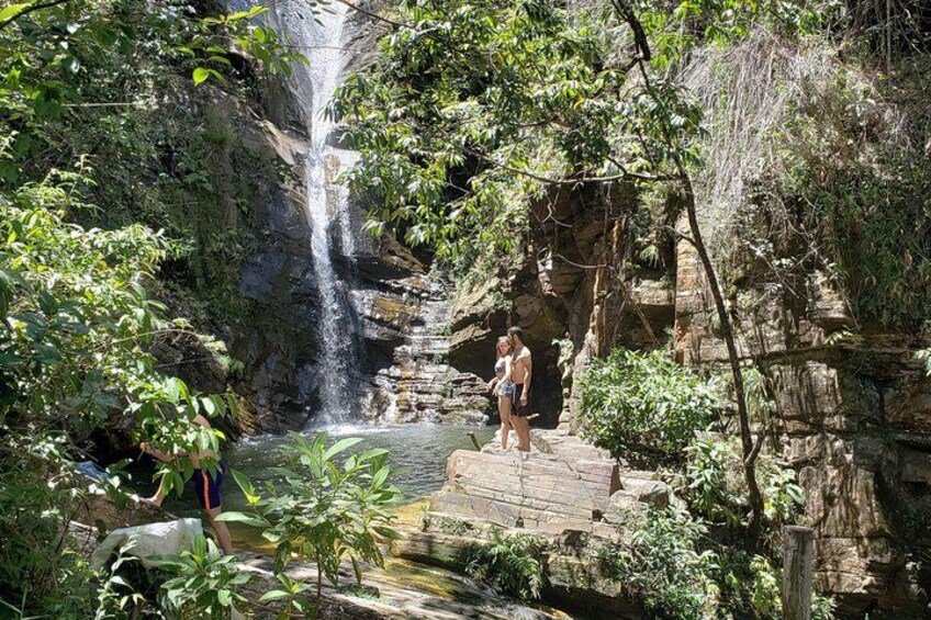 A waterfall cascading into a pool surrounded by lush greenery and rocky terrain. 1