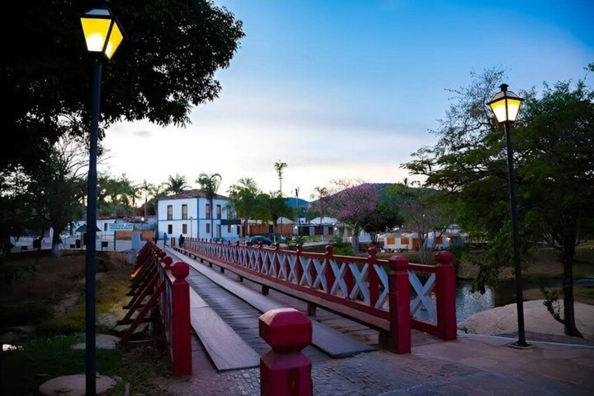 A wooden bridge with red railings, a paved walkway, and lamp posts. 4