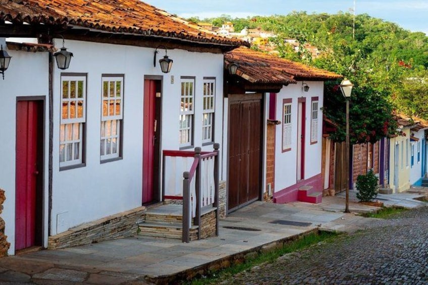A cobblestone street lined with colorful houses, a wooden staircase, and a hill in the background. 2