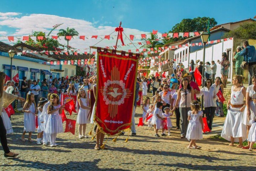 A parade with participants carrying a large red banner, a crowd of spectators, and buildings lining the street. 5