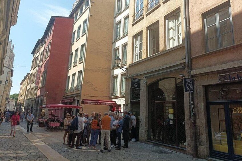 Una calle adoquinada con peatones, edificios y un toldo rojo. 1