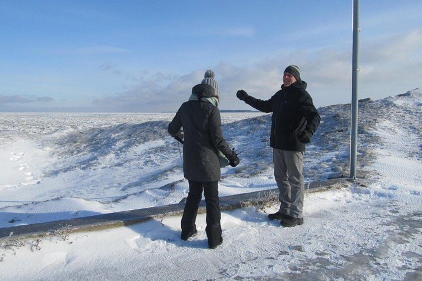 Twee personen staan op een besneeuwde heuvel met een metalen paal, met uitzicht op een vlak landschap. 3