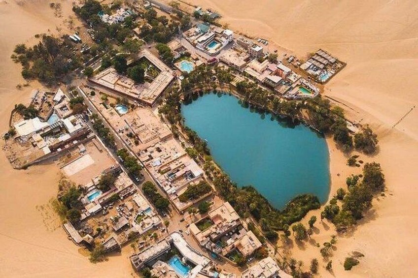 Oversigtsbillede af et resort med en stor pool omgivet af bygninger og sandklitter. 4