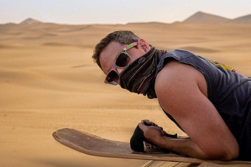 En person sidder på en træplade i en ørken med sandklitter i baggrunden. 5