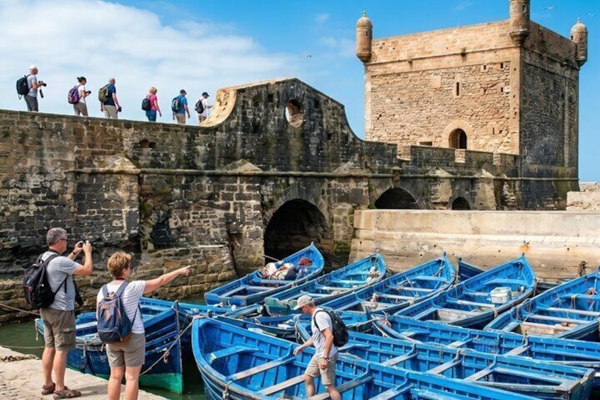 Des touristes se trouvent sur un pont de pierre historique, avec des bateaux amarrés en contrebas. 1