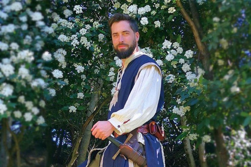 Una persona vestida con traje de época en un jardín con árboles de flores blancas. 5
