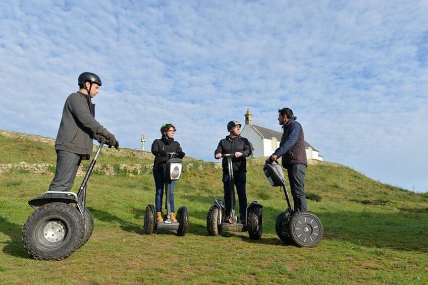 Four people on segways on a grassy hill with a white building in the background. 3
