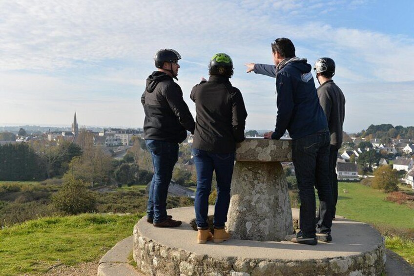 Four people standing on a stone platform overlooking a town with a church spire in the distance. 4
