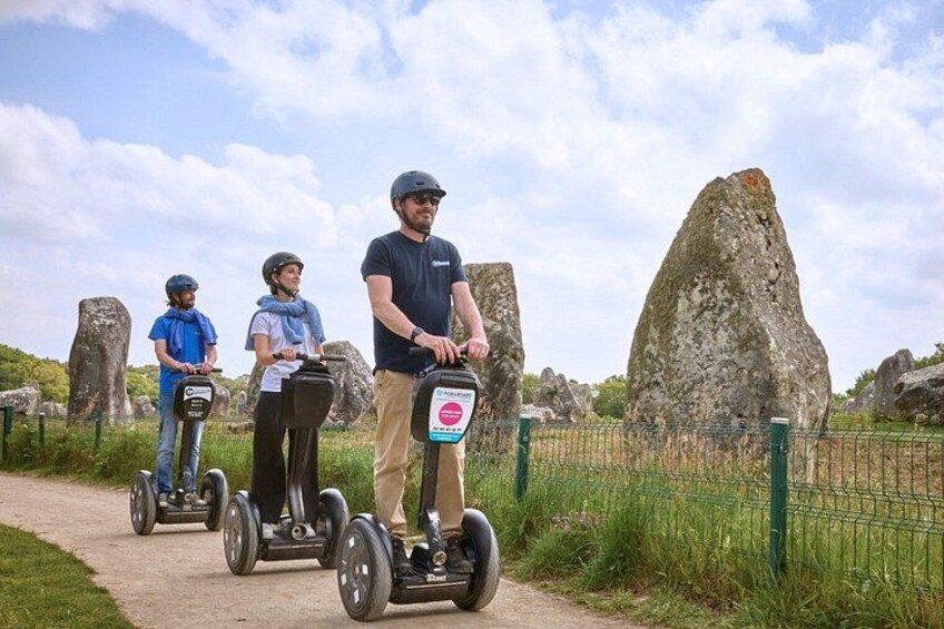Three people on segways on a path with large rocks and a green fence in the background. 1