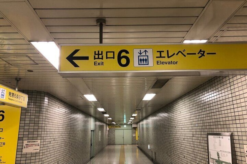 Una estación de metro con un letrero amarillo que indica la salida y el ascensor. 1