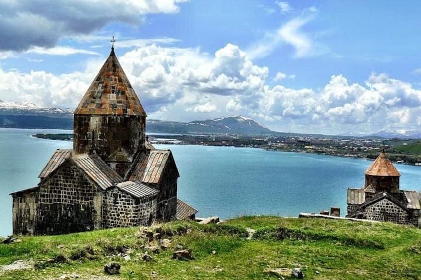 A church with a pointed roof and a smaller building with a dome, both made of stone, overlooking a calm lake with mountains in the distance. 4
