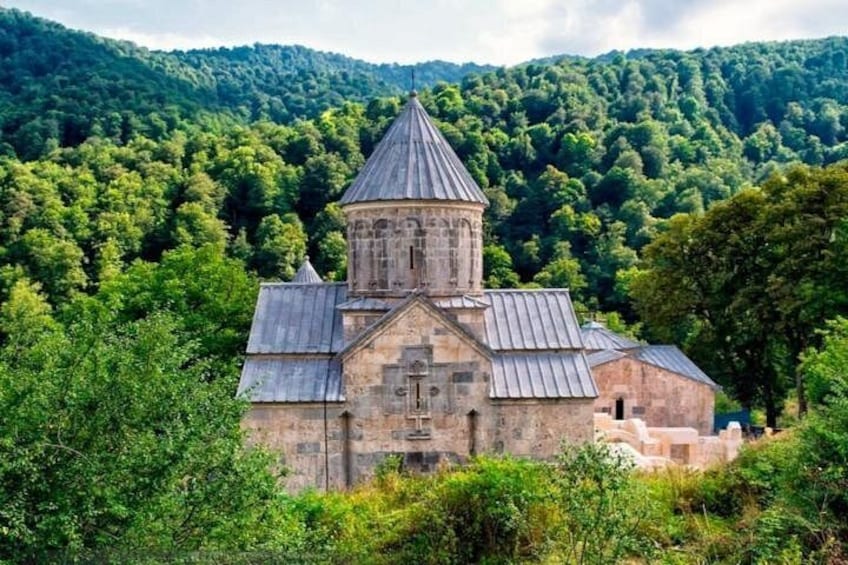 A stone church with a bell tower surrounded by lush green forest. 3