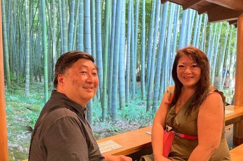 Two people seated at a wooden table with a bamboo forest in the background. 1