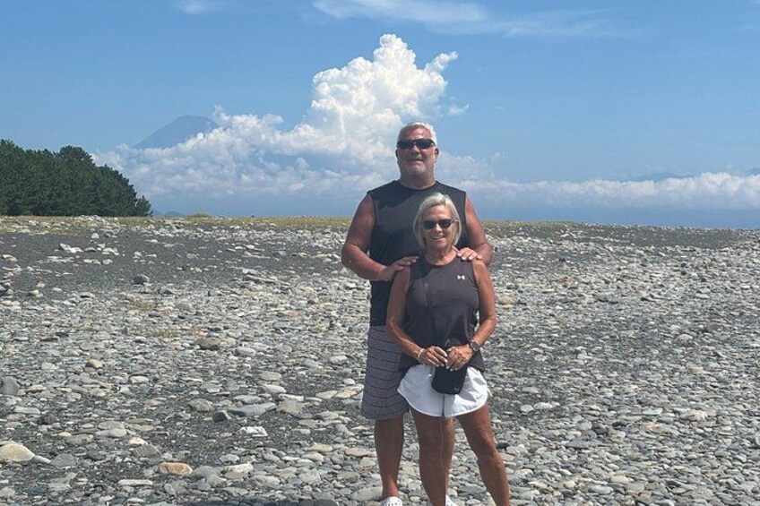 Two people standing on a rocky beach with a mountain in the background. 2