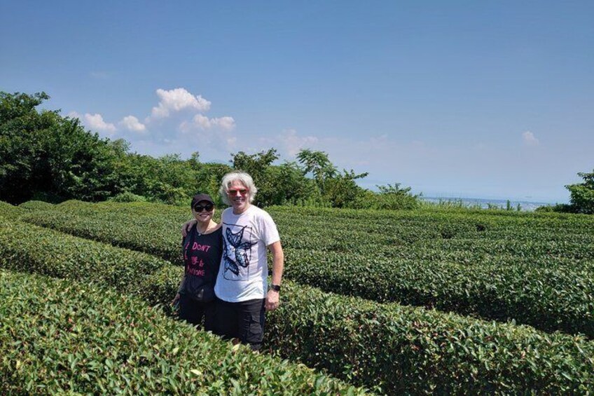Two people standing in a field of green plants, with trees and a clear sky in the background. 5