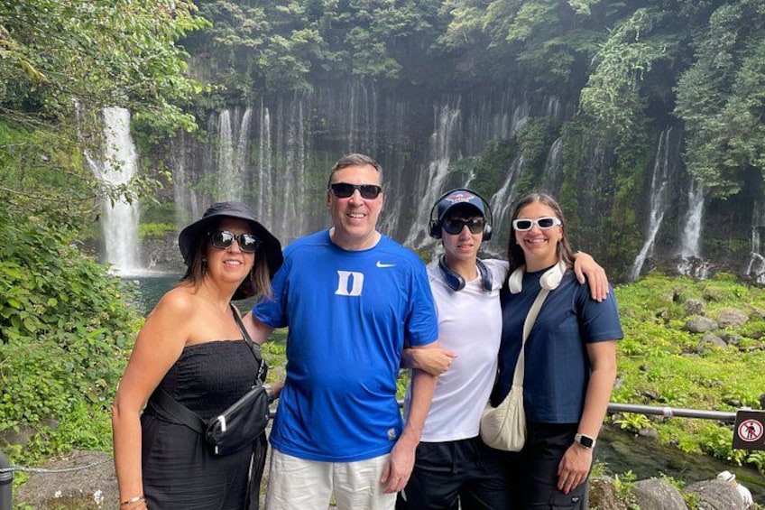 A group of people standing in front of a waterfall with lush greenery. 2